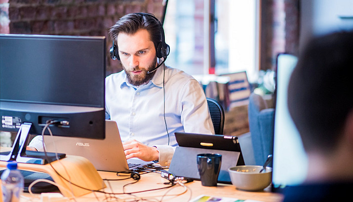 Mehrere Personen arbeiten im Büro an Notebooks; ein Mann trägt ein Headset – steht für die erfolgreiche Zusammenarbeit nach einer Microsoft Teams Schulung durch externen Dozenten